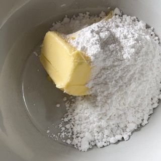 Un pezzo di burro è appoggiato su una ciotola di zucchero a velo.