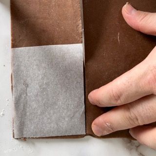 Una persona tiene in mano un pezzo di carta oleata sopra un pezzo di cioccolato.