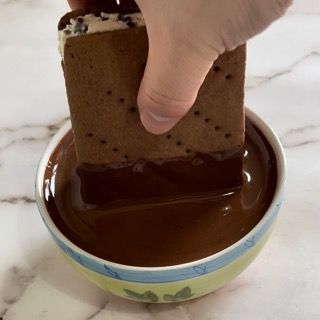 Una persona sta immergendo uno s'more in una ciotola di salsa al cioccolato