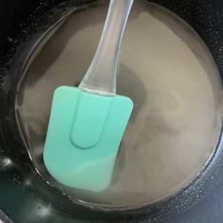 Una spatola verde è immersa in una pentola piena di liquido.