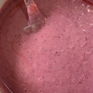 Un primo piano di una ciotola di liquido rosa con un cucchiaio dentro.