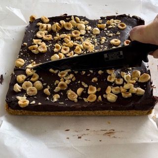 Una persona sta tagliando una fetta di torta al cioccolato con sopra delle noci