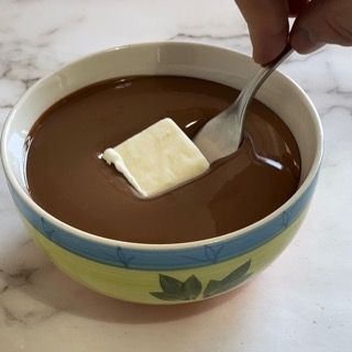 Una persona sta immergendo un pezzo di burro in una ciotola di salsa al cioccolato