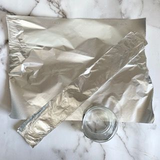 Un pezzo di carta stagnola e un bicchiere su un tavolo.