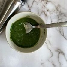 Una ciotola di salsa verde con un cucchiaio dentro su un tavolo.