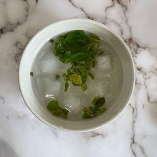 Una ciotola d'acqua con cubetti di ghiaccio e foglie verdi dentro