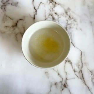 Una ciotola bianca piena di liquido è appoggiata su una superficie di marmo.