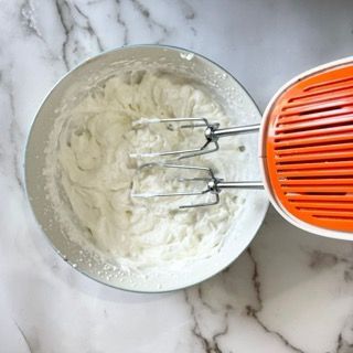 Una ciotola di panna montata accanto a una planetaria su un tavolo.