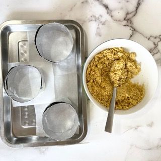 Una ciotola di cibo con un cucchiaio dentro accanto a un vassoio di pirottini da forno