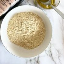 Una ciotola di farina è appoggiata su un tavolo accanto a una bottiglia di olio d'oliva.