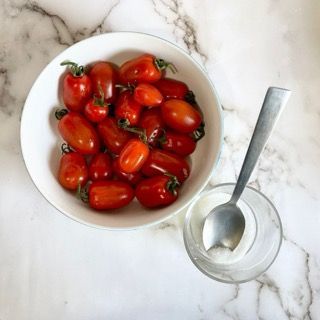 Una ciotola di pomodori accanto a un bicchiere con un cucchiaio dentro