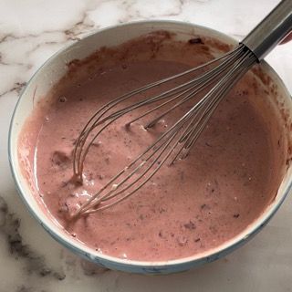 Una ciotola di liquido rosa con una frusta dentro.