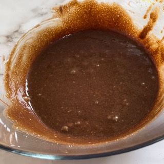 Su un tavolo c'è una ciotola di vetro piena di liquido marrone.