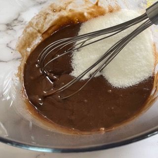 Una frusta è in una ciotola di cioccolato e zucchero.