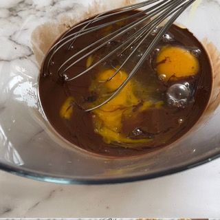 Una ciotola di salsa al cioccolato con uova e una frusta dentro.