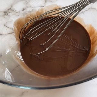 Una frusta è in una ciotola di salsa al cioccolato.