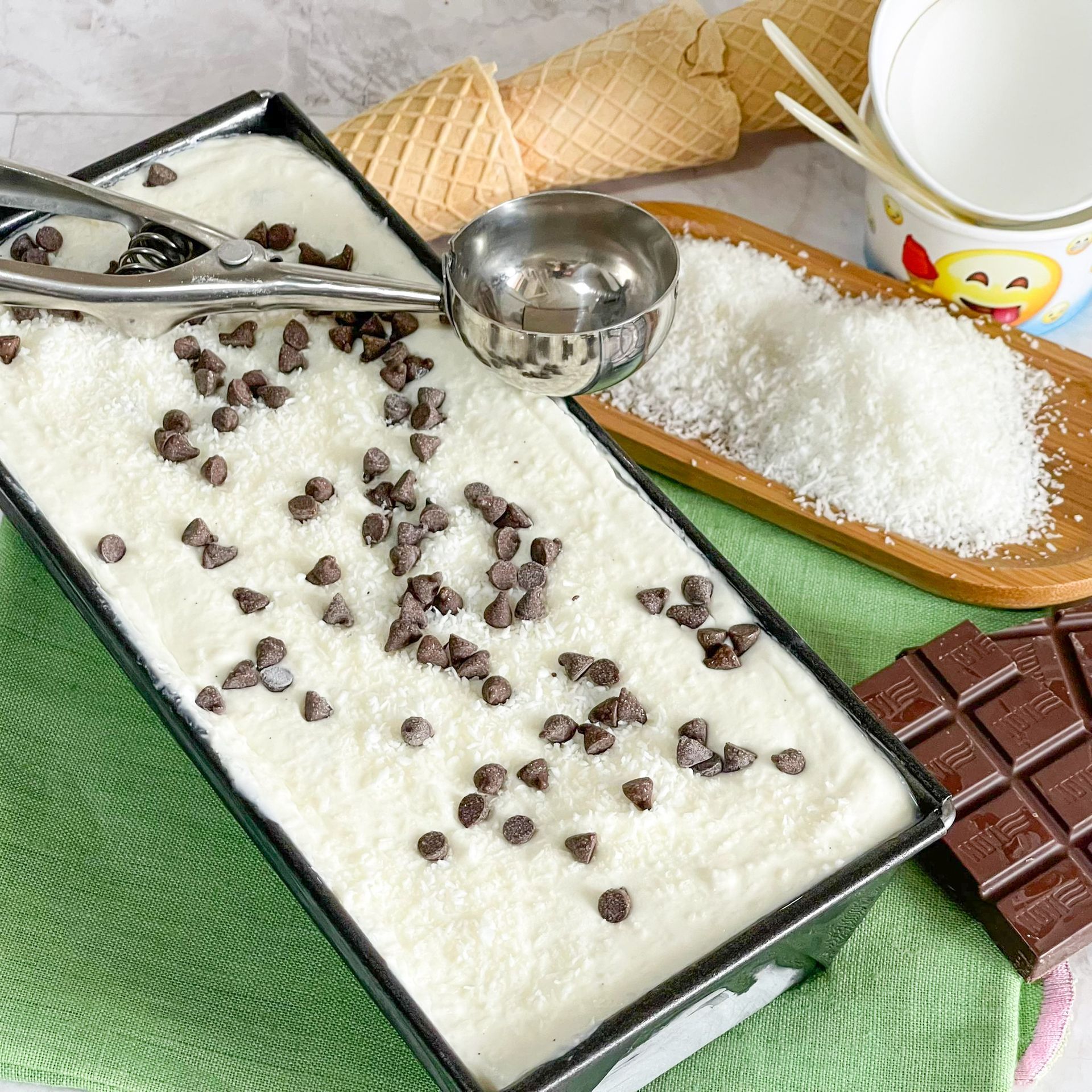 Un contenitore di gelato con gocce di cioccolato e una pallina su un tavolo.