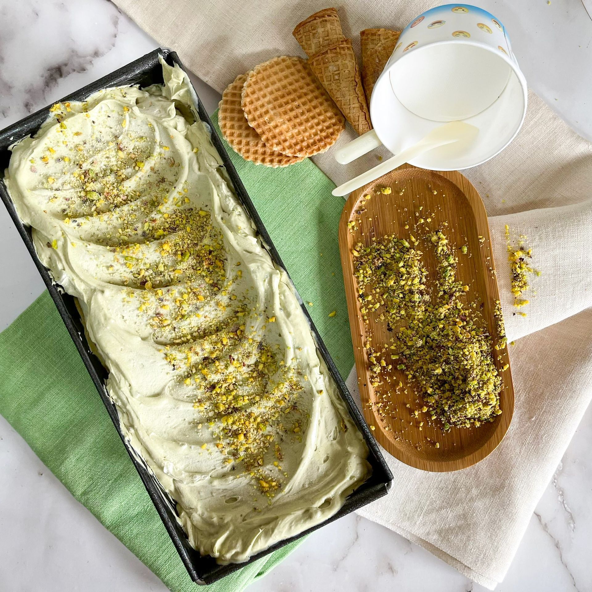 Un contenitore di gelato al pistacchio è appoggiato su un tavolo accanto a una ciotola di legno.