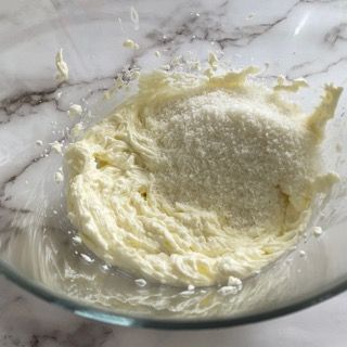 Una ciotola di vetro piena di panna montata e cocco su un tavolo.