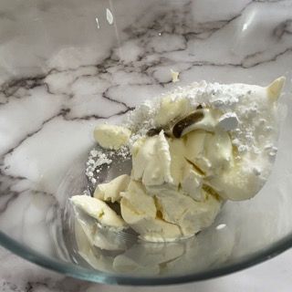 Una ciotola di vetro piena di panna montata e zucchero a velo su un tavolo.