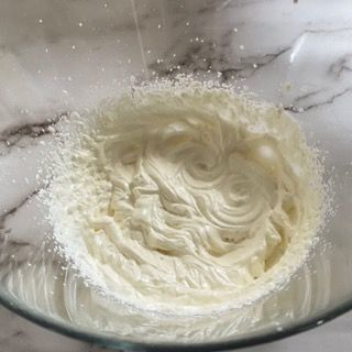 Una ciotola di vetro piena di panna montata e zucchero a velo.