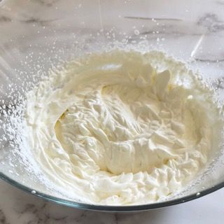 Una ciotola di vetro piena di panna montata su un tavolo.