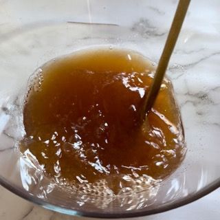 Una ciotola di vetro piena di un liquido marrone con un cucchiaio dentro