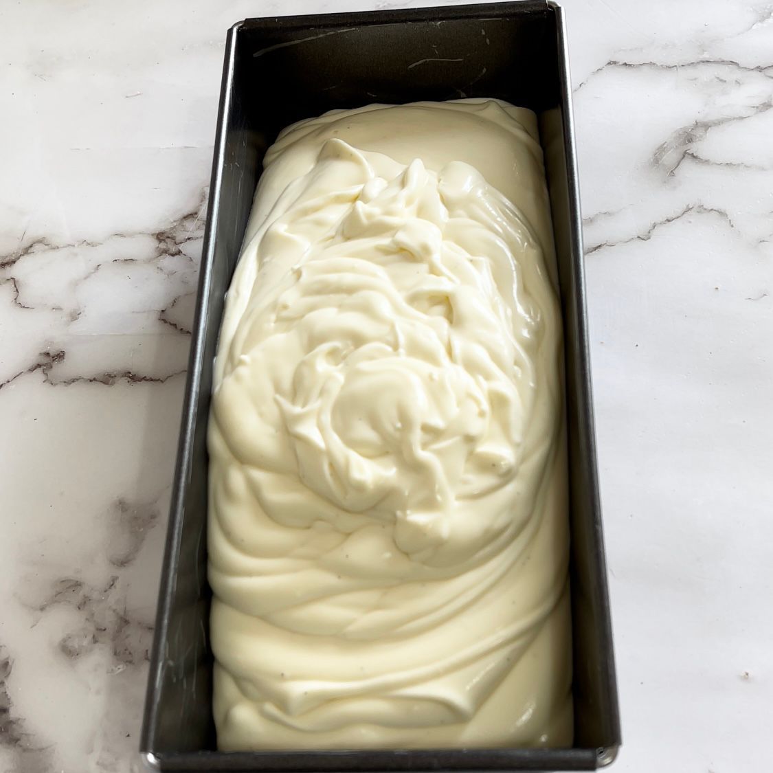 Uno stampo da plumcake riempito di glassa bianca su una superficie di marmo.