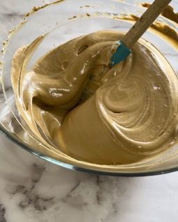 Una ciotola di vetro piena di un liquido marrone con una spatola dentro.