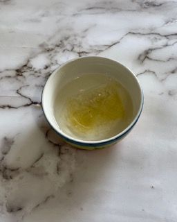 Una piccola ciotola piena di liquido è appoggiata su un tavolo di marmo.