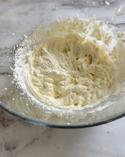 Una ciotola di vetro piena di panna montata su un tavolo.