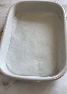 Una teglia bianca riempita di carta oleata su un tavolo.