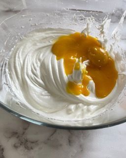 Una ciotola di vetro piena di panna montata e un liquido giallo.