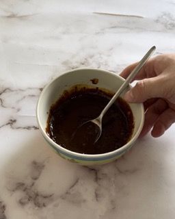 Una persona tiene in mano una ciotola di salsa con un cucchiaio dentro.