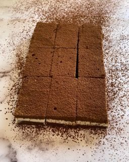 Un pezzo di torta al cioccolato viene tagliato a quadratini e ricoperto di cioccolato in polvere