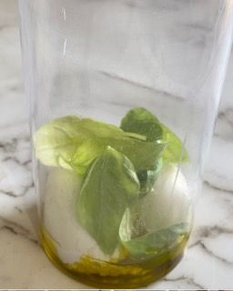 Un bicchiere pieno di foglie di basilico e olio d'oliva su un tavolo.