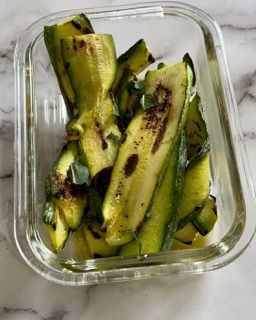 Un contenitore di vetro pieno di zucchine affettate su un tavolo.