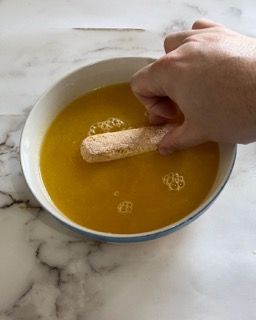 Una persona sta immergendo un bastoncino di pollo in una ciotola di salsa.