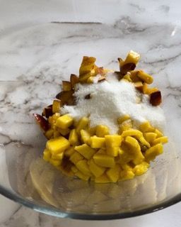 Una ciotola di vetro piena di frutta tritata e zucchero su un tavolo.