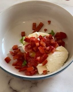 Una ciotola bianca piena di pomodori e maionese su un tavolo.