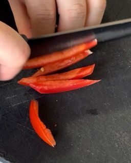 Una persona sta tagliando un peperone rosso su un tagliere