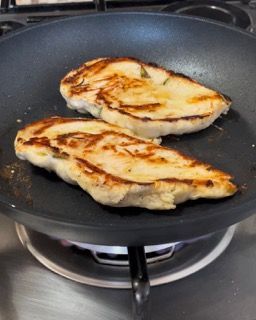 Due petti di pollo stanno cuocendo in una padella sul fornello