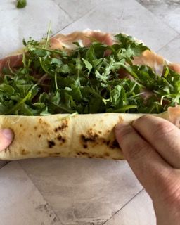 Una persona tiene in mano un taco con lattuga e prosciutto