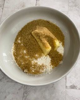 Una ciotola bianca piena di zucchero di canna e due pezzetti di burro.