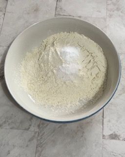 Una ciotola bianca piena di farina e sale su un pavimento piastrellato.