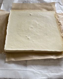 Un pezzo di formaggio è appoggiato su un foglio di carta oleata.