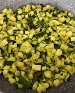 Una padella piena di zucchine e cipollotti tritati.