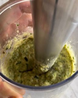 Una persona sta usando un frullatore per preparare una salsa in un bicchiere.