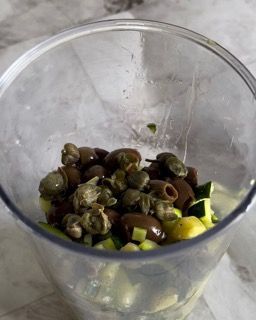 Una ciotola trasparente piena di olive e cetrioli su un tavolo.