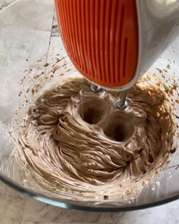 Un mixer sta mescolando la glassa al cioccolato in una ciotola di vetro.